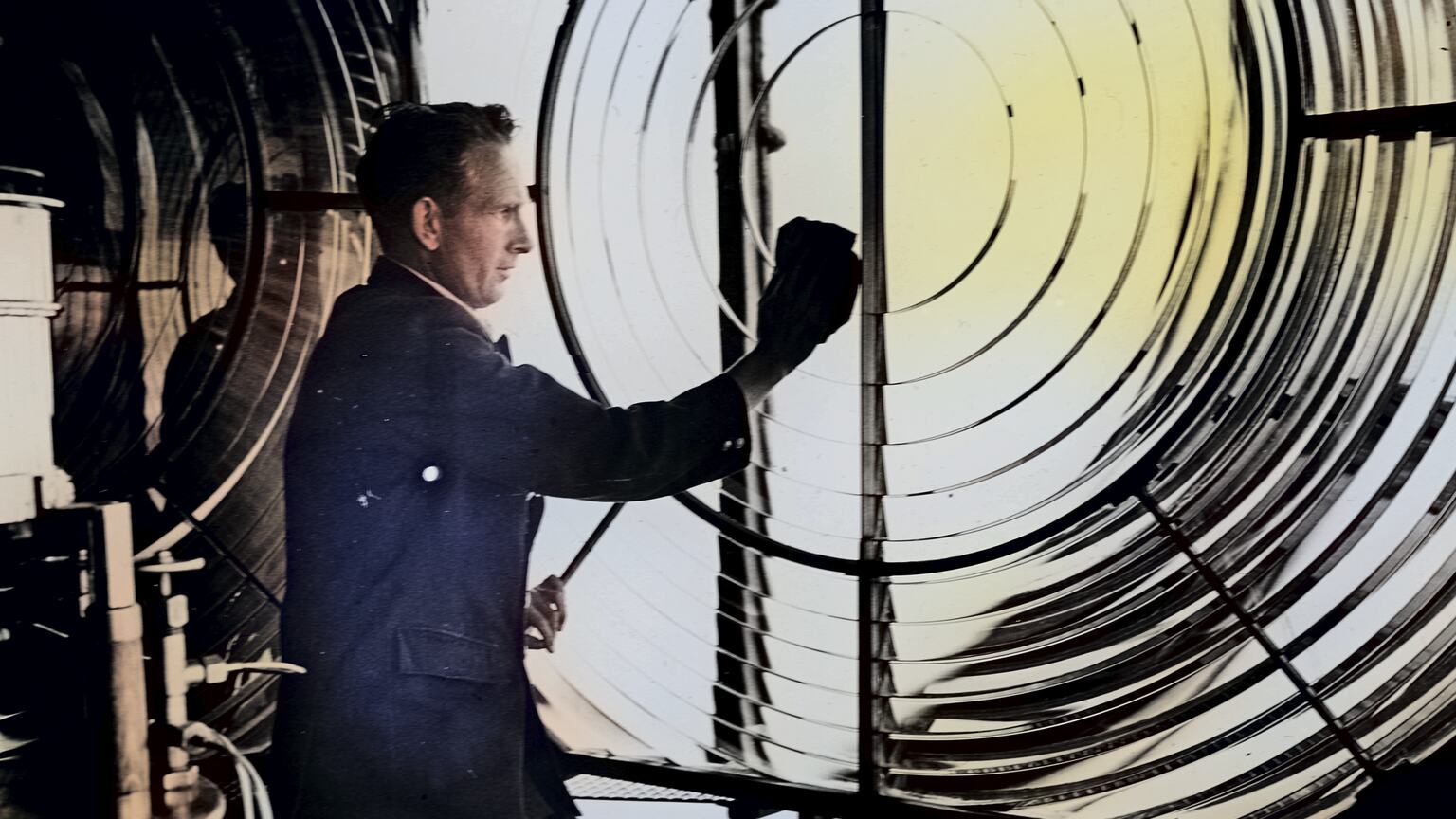 Man in dark suit cleaning a large Fresnel lens inside a lighthouse