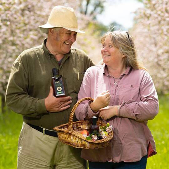 Rod and Julie from Highbank walking through a blooming orchard, carrying a basket of local produce and products